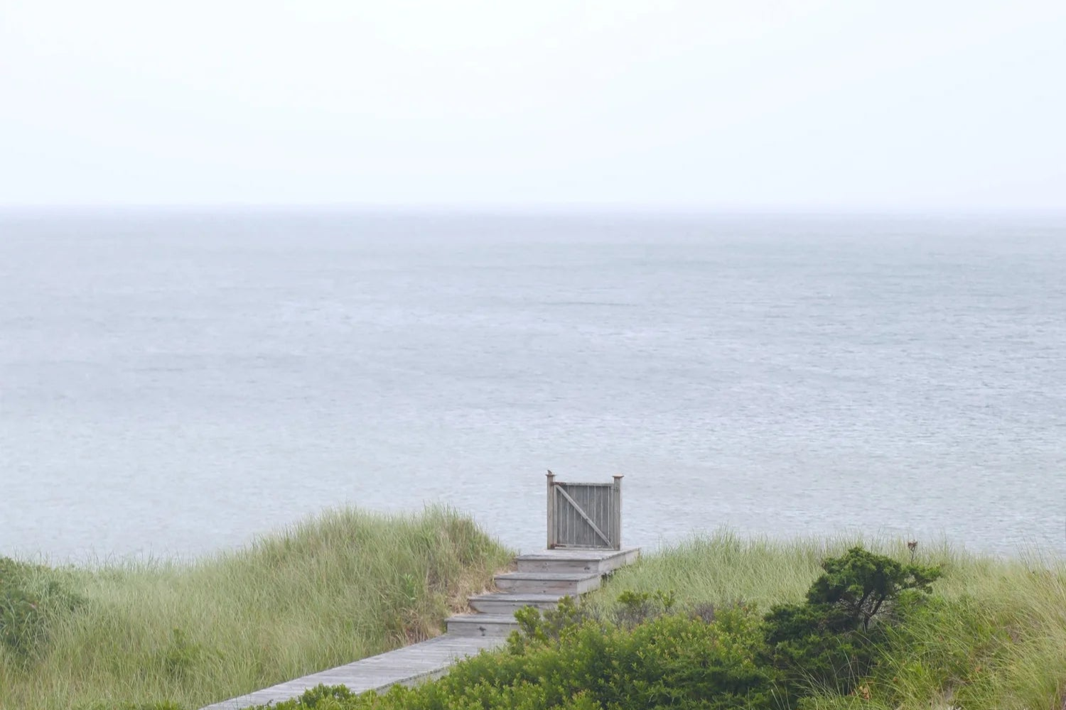 Wooden pathway leading to a wooden door on a grassy dune with ocean in the background